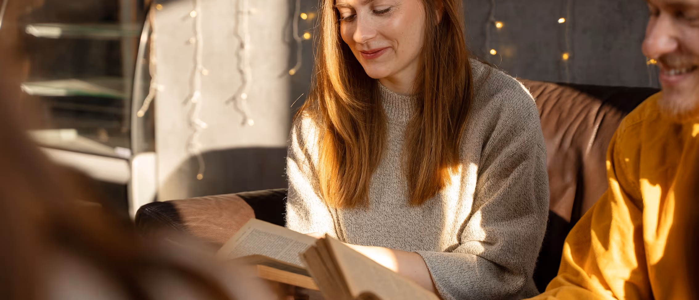 A woman reading a book aloud to others on a couch
